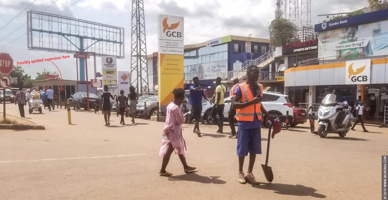 Ghana Prisoner in Orange Hazard Vest on top of a Blue Uniform Holding A Shovel and Panhandling for Money on the Street of Accra, Ghana. © 2019 Muntaka Chasant