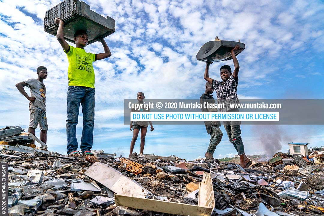 Child labour in Africa: Osei (right), 15 years old, is about to smash an old CRT TV against a rock to recover the iron materials inside at Agbogbloshie, Ghana. Fourteen-year-old Ankrah in a lime green t-shirt with “I can do it!” on the front is waiting for his turn. More than 70 million children in Africa are estimated to be in child labour. © 2020 Muntaka Chasant