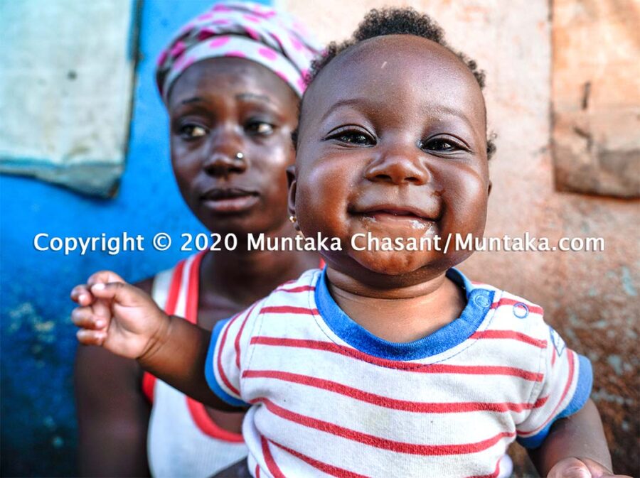An infant smiles against her hopeless urban poor mother. Copyright © 2020 Muntaka Chasant.