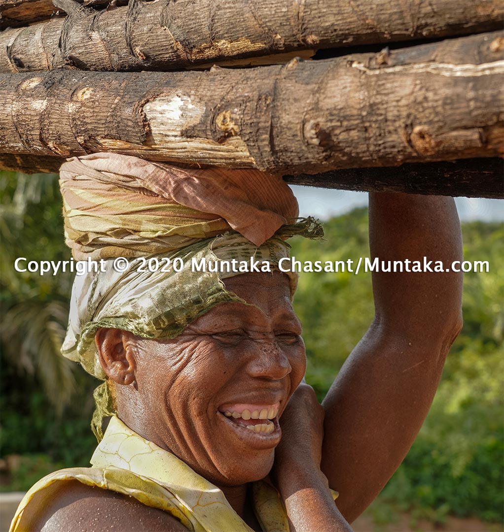 Rural Poverty in Ghana: A 50 years old rural poor woman smiles as she carries fuelwood on her head near the Cape Three Points in Ghana, the nearest land to 0 latitude, 0 longitude, and 0 altitude (also null island). Copyright © 2020 Muntaka Chasant