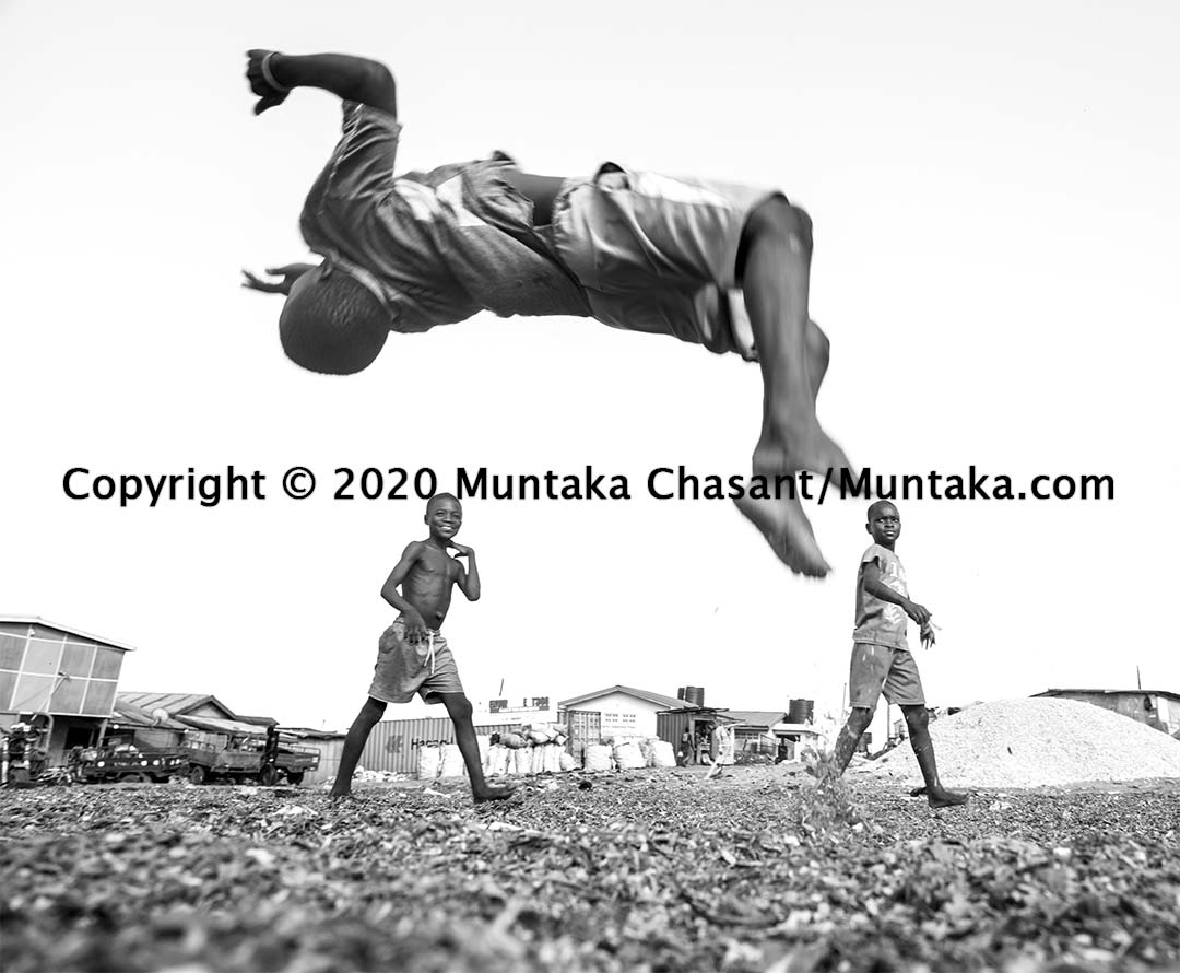 Slum children playing: Boy doing a backflip. Urban poor children had been backflipping and landing on sawdust. Copyright © 2020 Muntaka Chasant