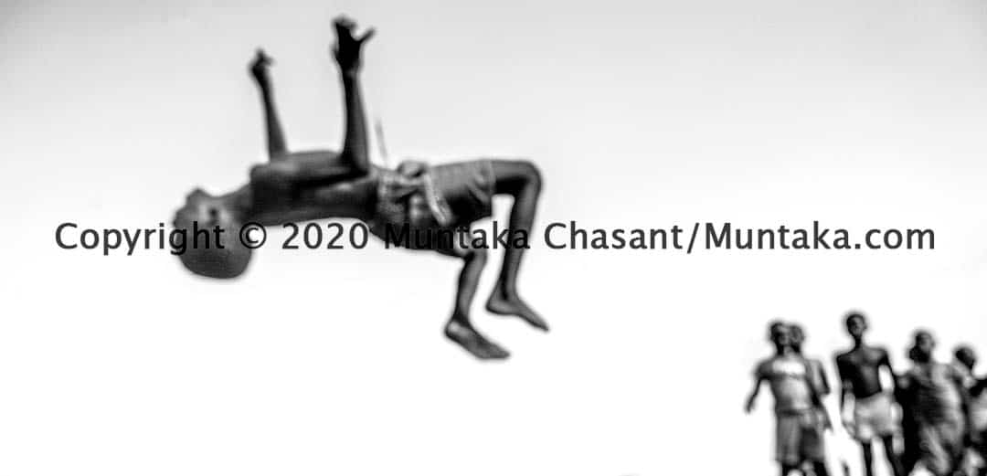 Slum children playing: Urban poor boy doing a backflip as other children watch. With no playgrounds, these Sodom and Gomorrah slum children have no choice but to play on rubbish-strewn sawdust piles. Copyright © 2020 Muntaka Chasant