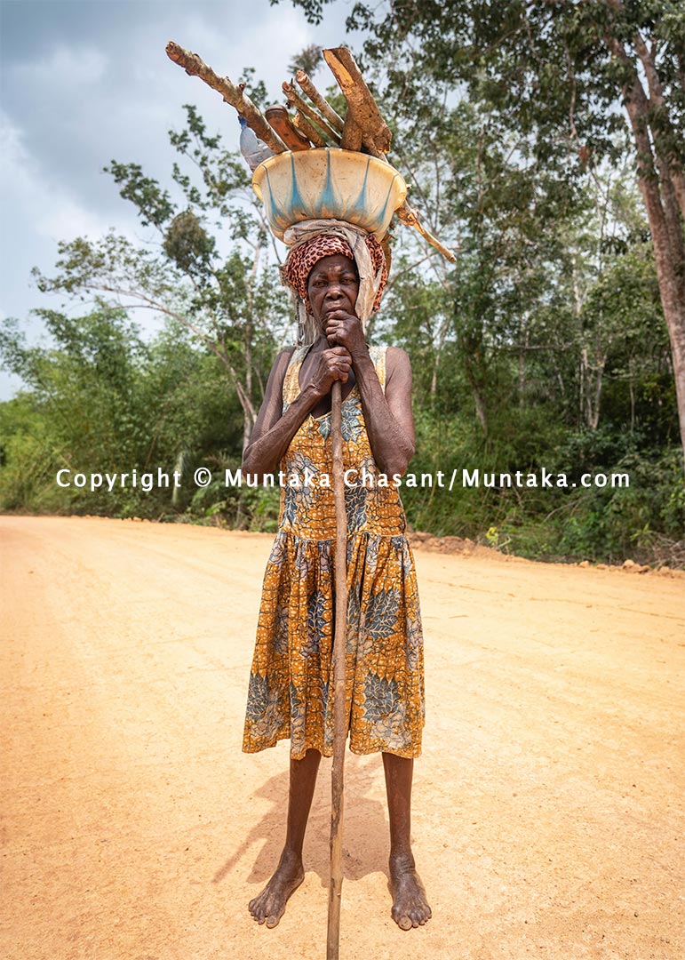 Poverty in Ghana: Elderly rural poor woman from the farm walks barefooted on a dirt road. Copyright © 2021 Muntaka Chasant