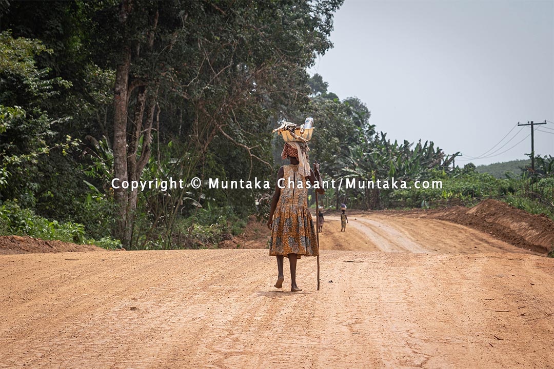 Elderly rural poor woman from the farm walks barefooted on a dirt road in rural Ghana. Copyright © 2021 Copyright © 2021 Muntaka Chasant