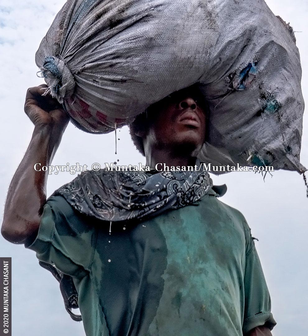 Human suffering: Poor man carries a plastic sack on his head with liquid dripping from it. More than 700 million people worldwide live on less than $2 a day. © 2020 Muntaka Chasant