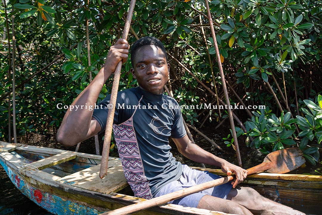 A young lagoon fisherman in an artisanal canoe holds onto a red mangrove root, southwest Ghana. Copyright © Muntaka Chasant
