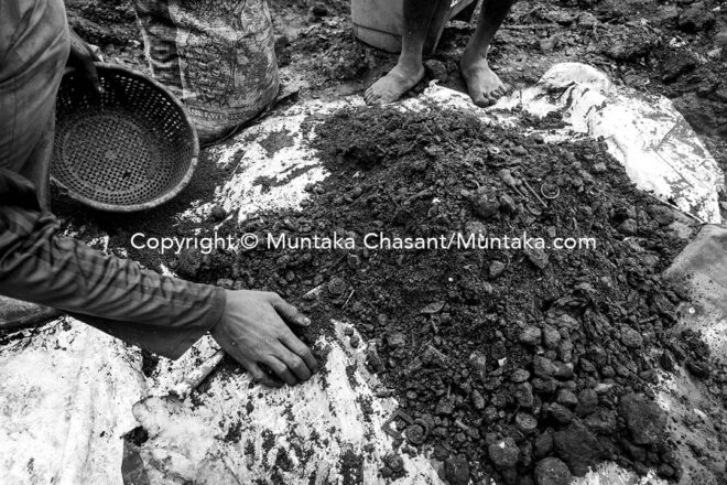 Separating dirt from rusted scrap metal recovered after digging deep into the surface of the demolished site. Copyright © Muntaka Chasant